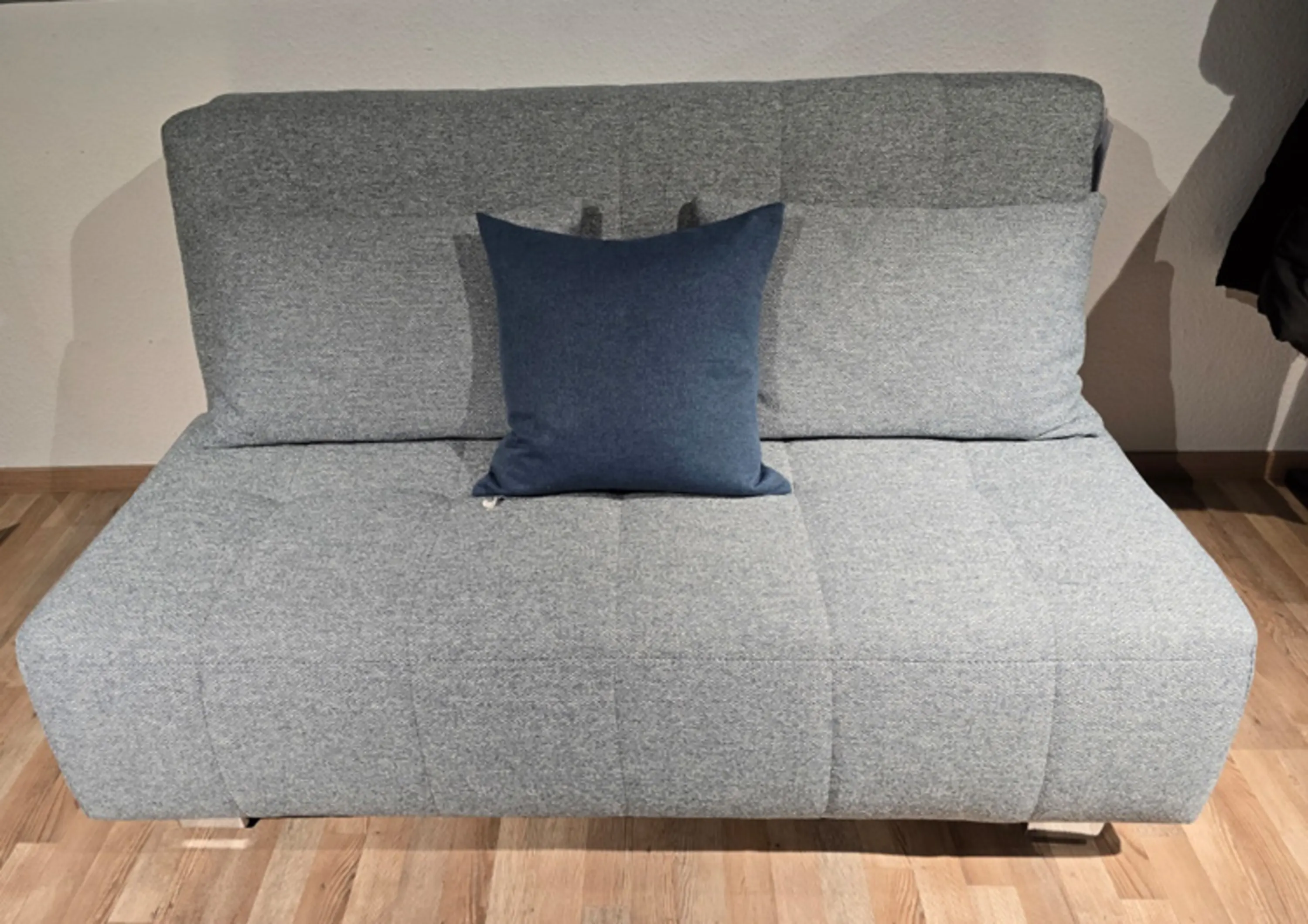Grau gepolstertes Schlafsofa, das mit einem einzelnen dunkelblauen Kissen auf der Sitzfläche dekoriert ist.