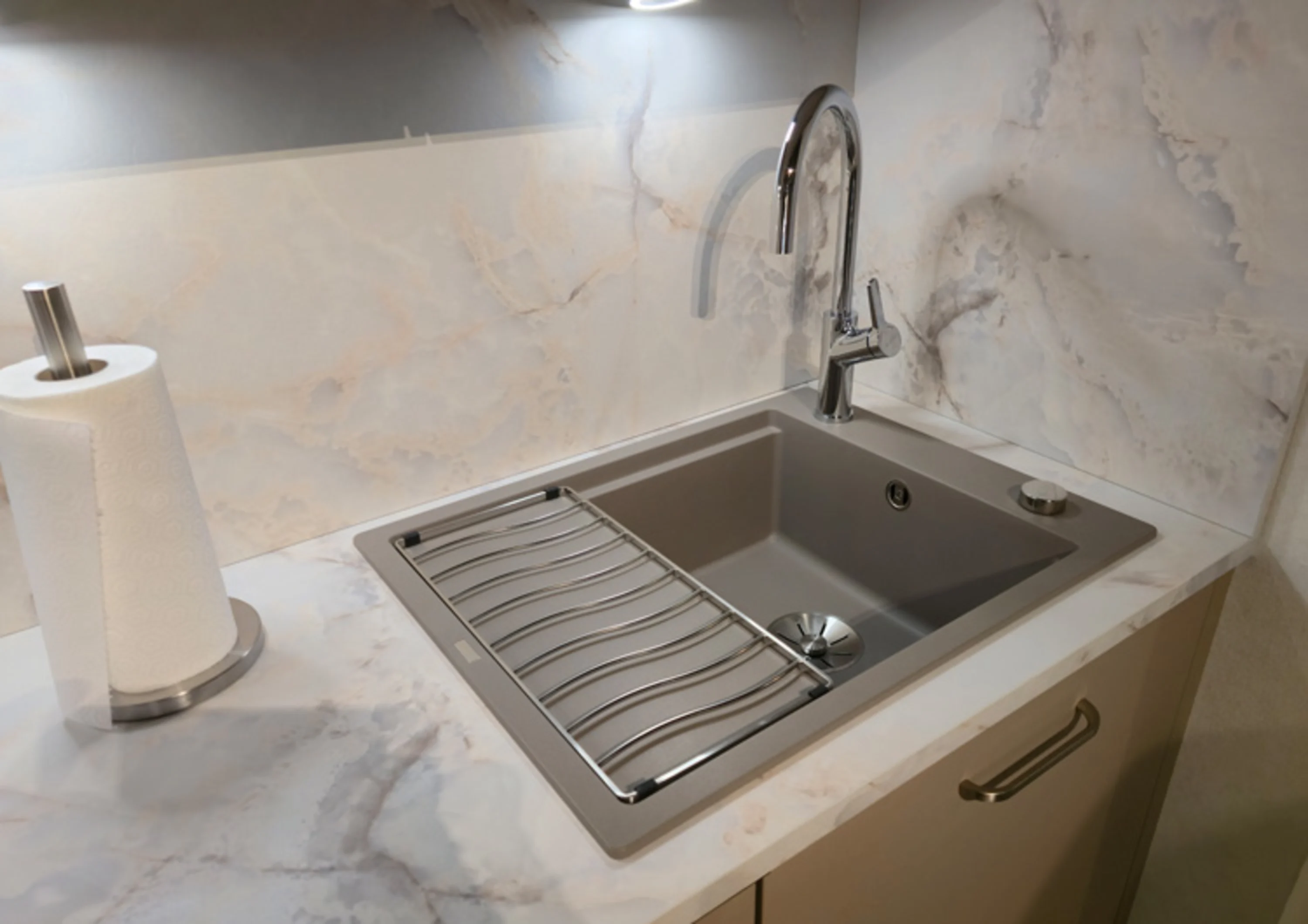 Das Bild zeigt ein modernes Spülbecken in einer Arbeitsplatte mit Marmor-Optik. Das Becken ist rechteckig und in Grau gehalten, mit einem hohen, verchromten Wasserhahn. Auf dem Becken liegt ein Abtropfgitter aus Metall.