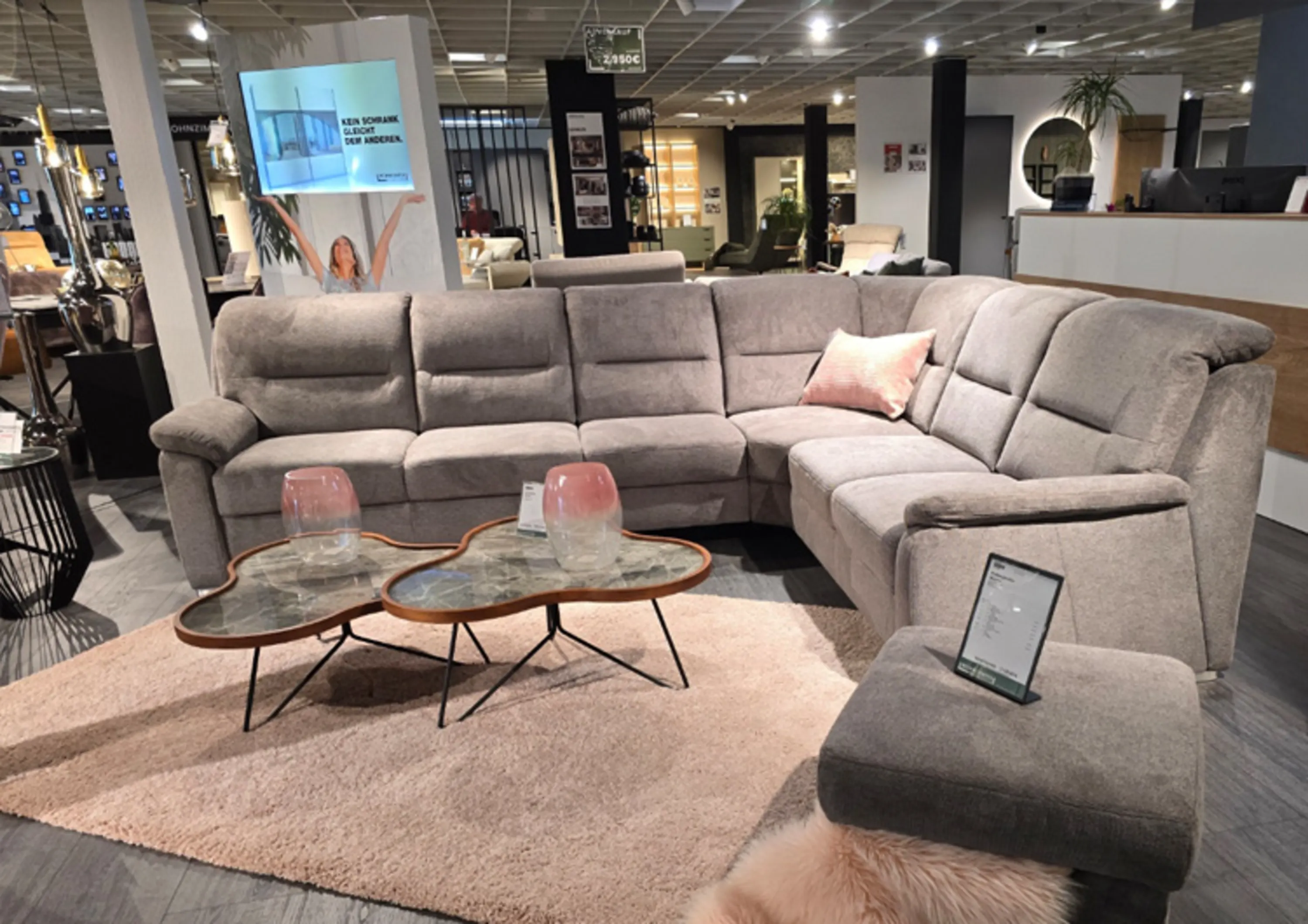 Graue klassische Stoff- Polstergarnitur in L-Form plus Hocker und Kissen.