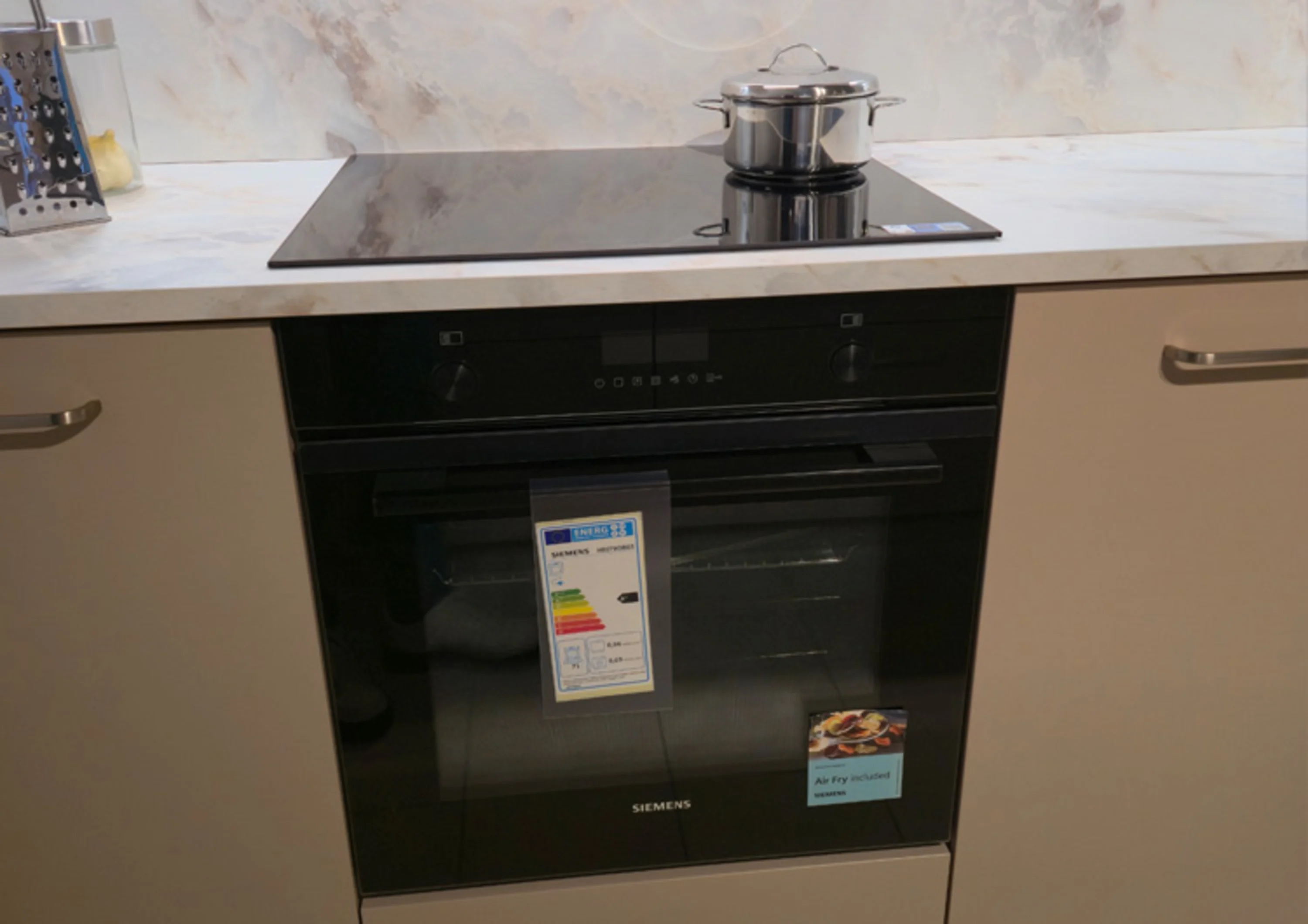 Das Foto zeigt eine moderne Kücheneinheit mit einem Siemens Einbaubackofen und einem Induktionskochfeld in schwarzer Glasoptik.