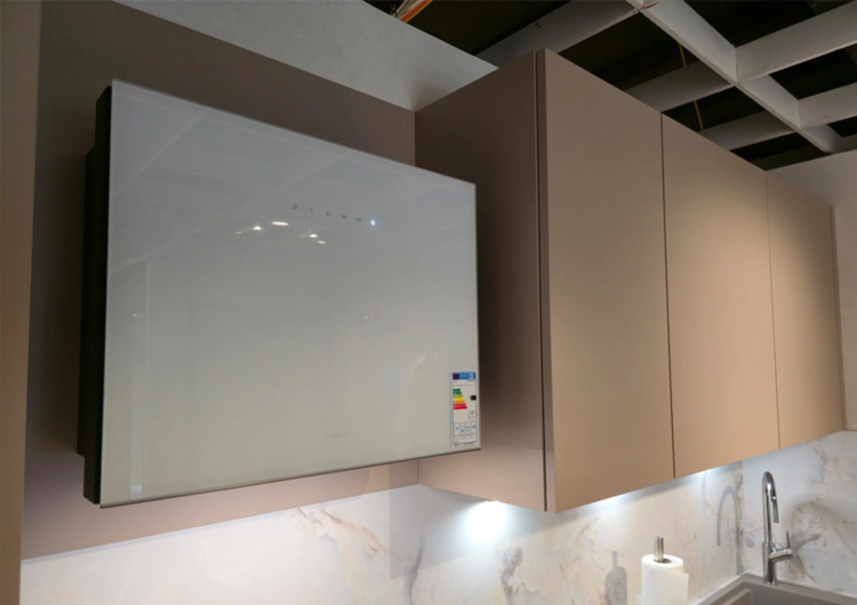 Das Bild zeigt einen modernen Küchenbereich mit Hängeschränken in einer matten Farbgebung. An der linken Seite ist ein Dunstabzugshaube mit einer glänzenden weißen Front angebracht.