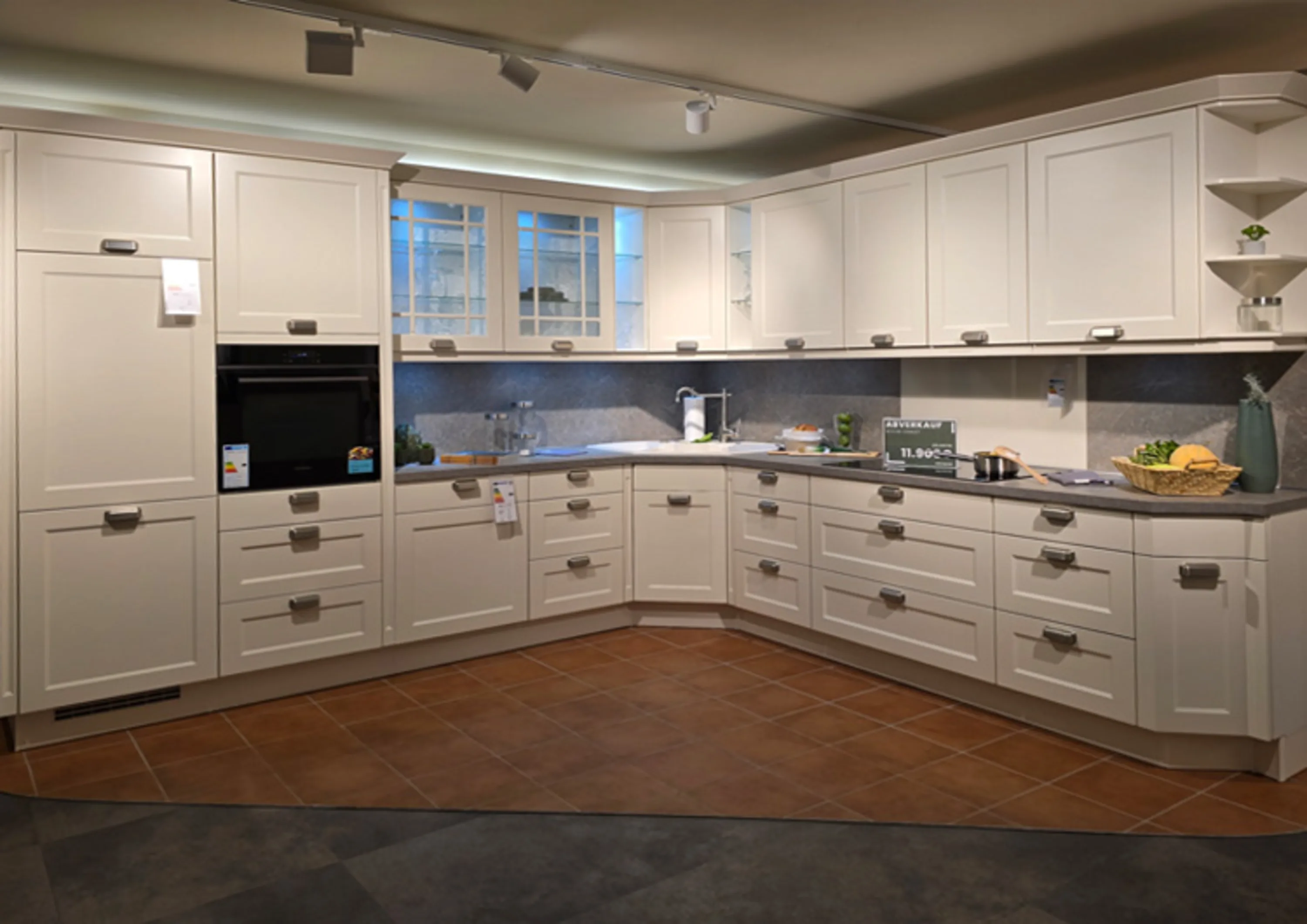 Eine große, L-förmige Einbauküche im klassischen Stil mit weißen Rahmenfronten und einer grauen Arbeitsplatte.