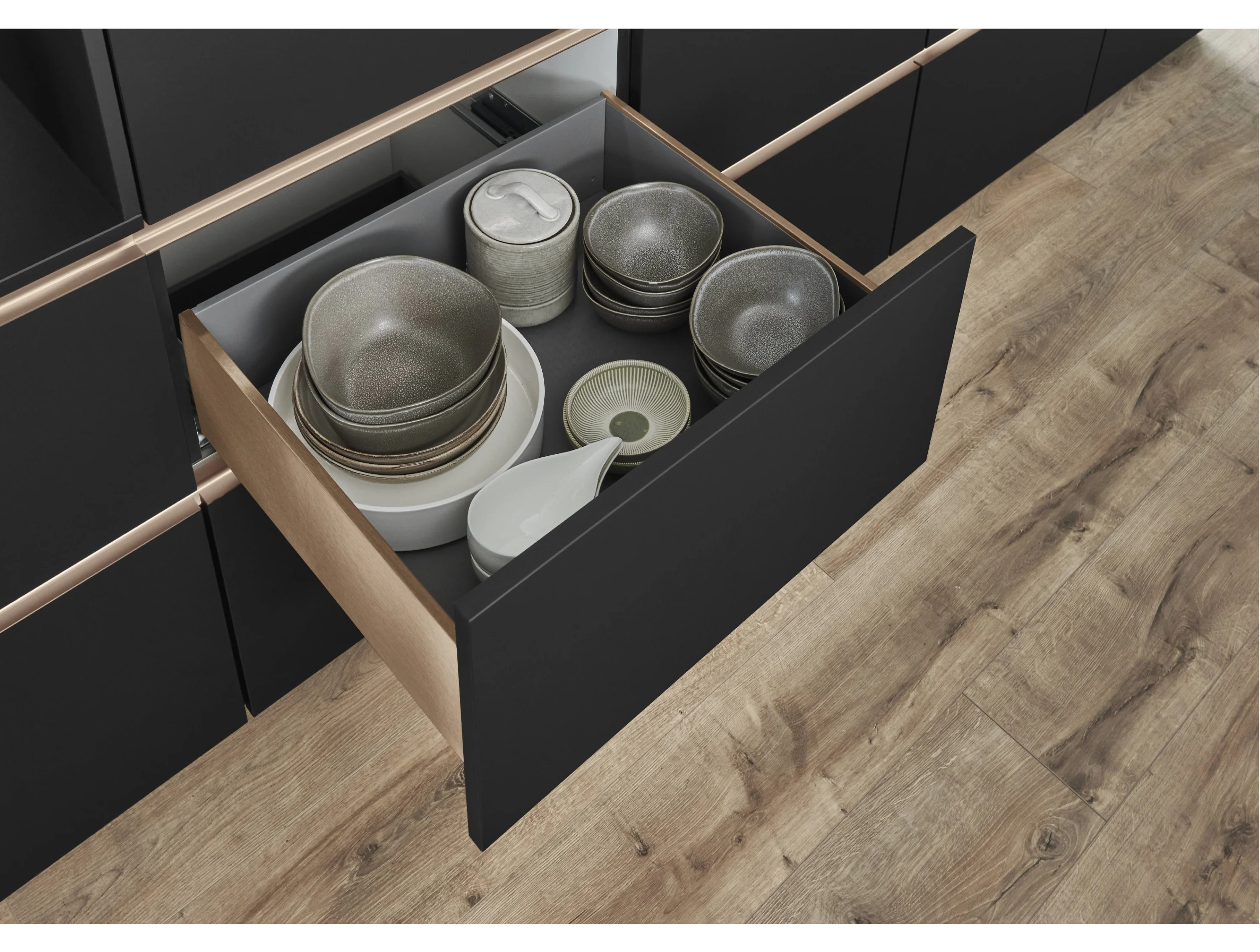 Kleiner offerner Schubkasten mit Geschirr in einer dunklen Küche mit beleuchteten Griffleisten