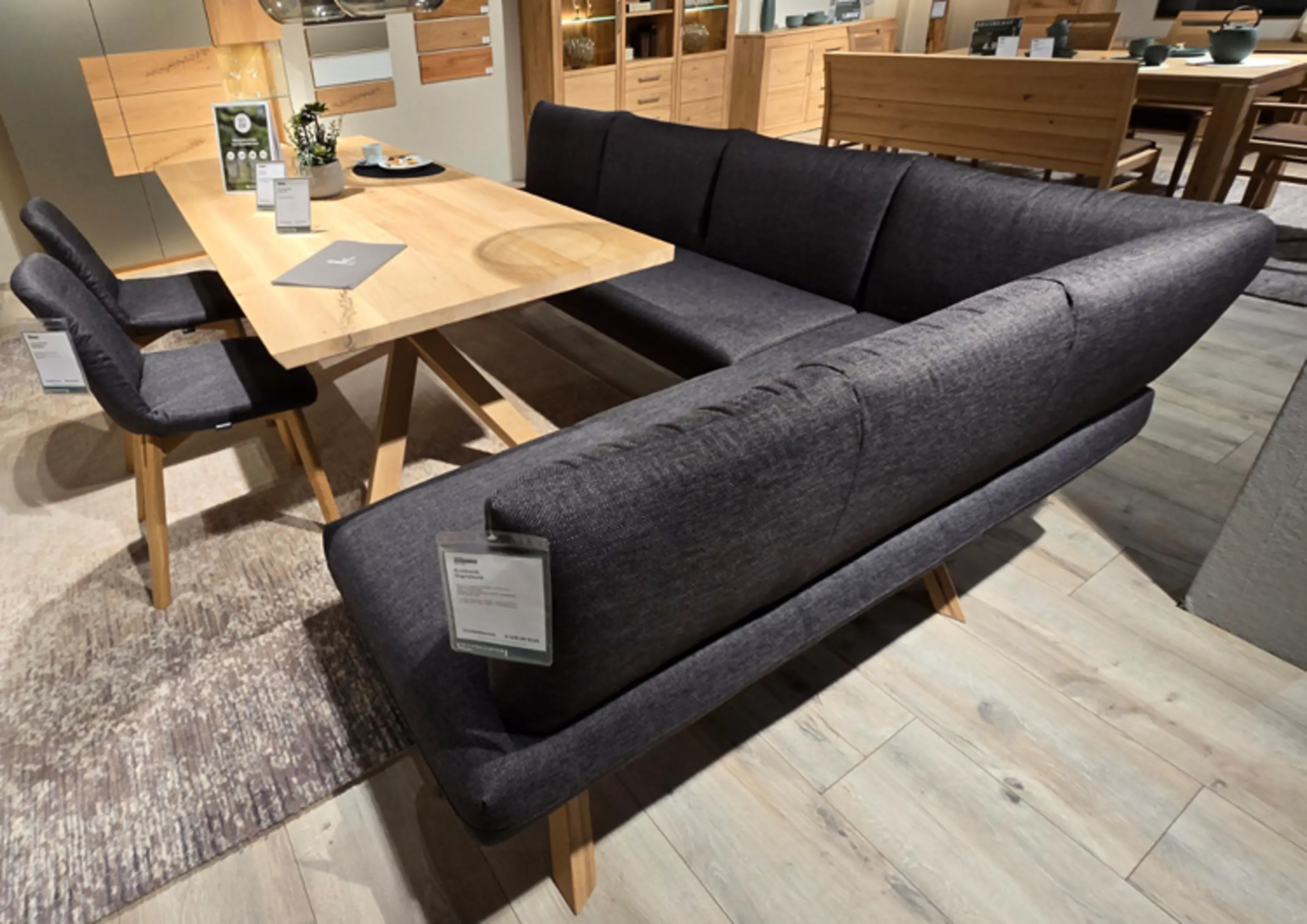 Eckbank mit Stoffbezogen Holzgestell. Im Hintergund ein Holztisch und zwei Stühle