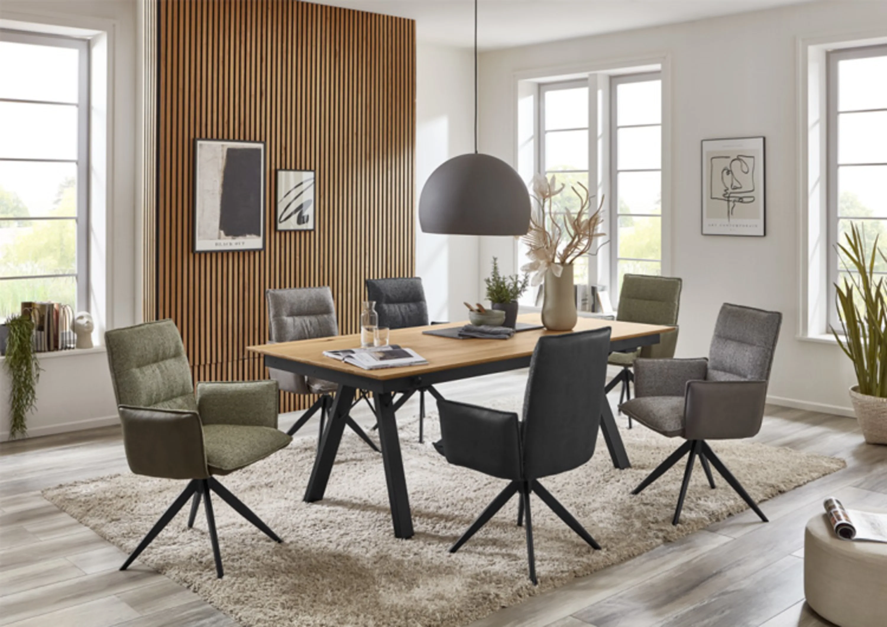 Sechs Esszimmerstühle mit Armlehne in verschiedenen Farben um einen Esstisch mit schwarzem Gestell