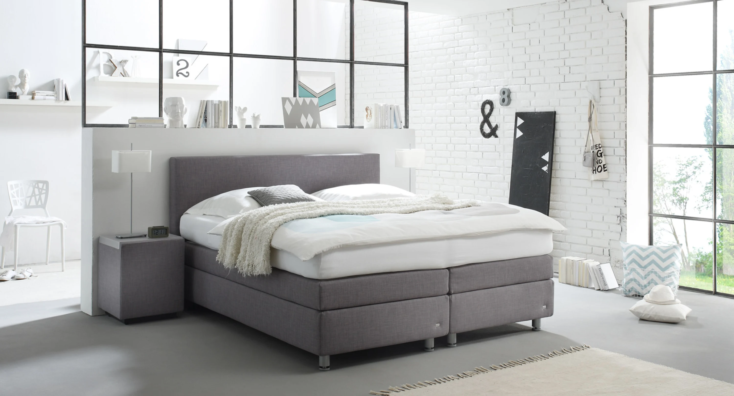 Graues Boxspringbett mit Nachtschrank in einem hellen Schlafzimmer