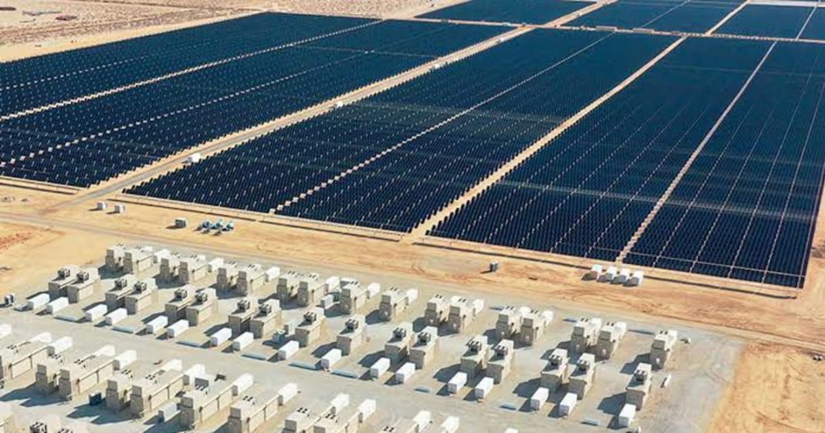 Solar panels stretching across Chile's Atacama Desert with wind turbines visible in distance