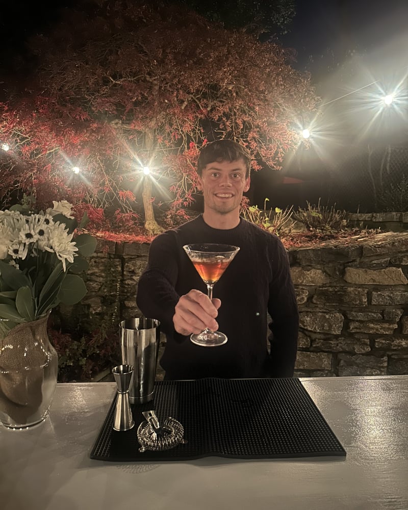 Eddie Gady of 513Sips presenting a finished cocktail behind the bar at an evening event