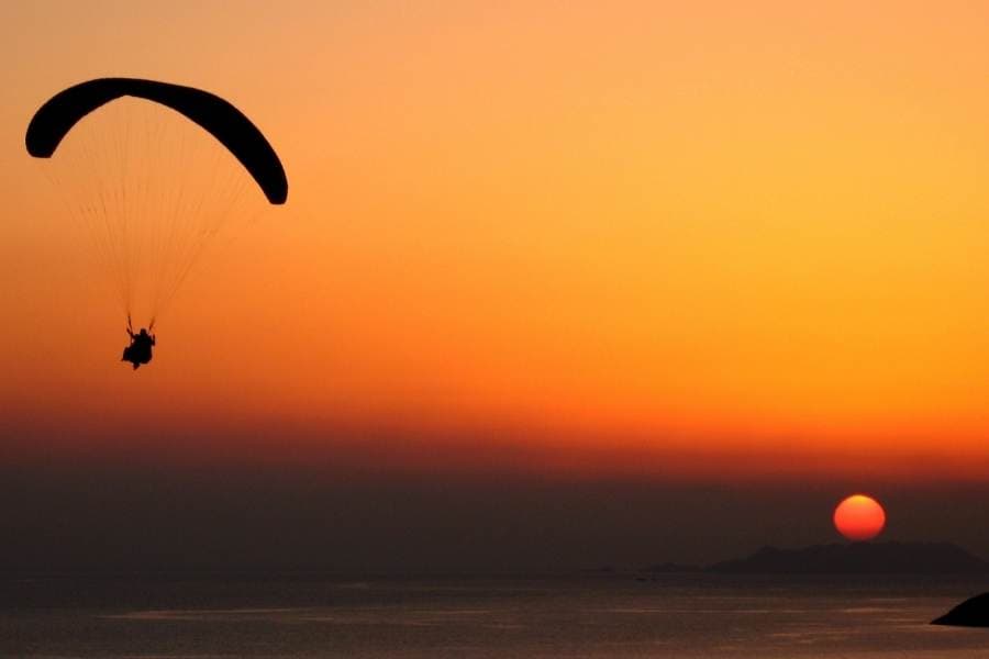 silhouette of a paraglider in the air with a sunset background