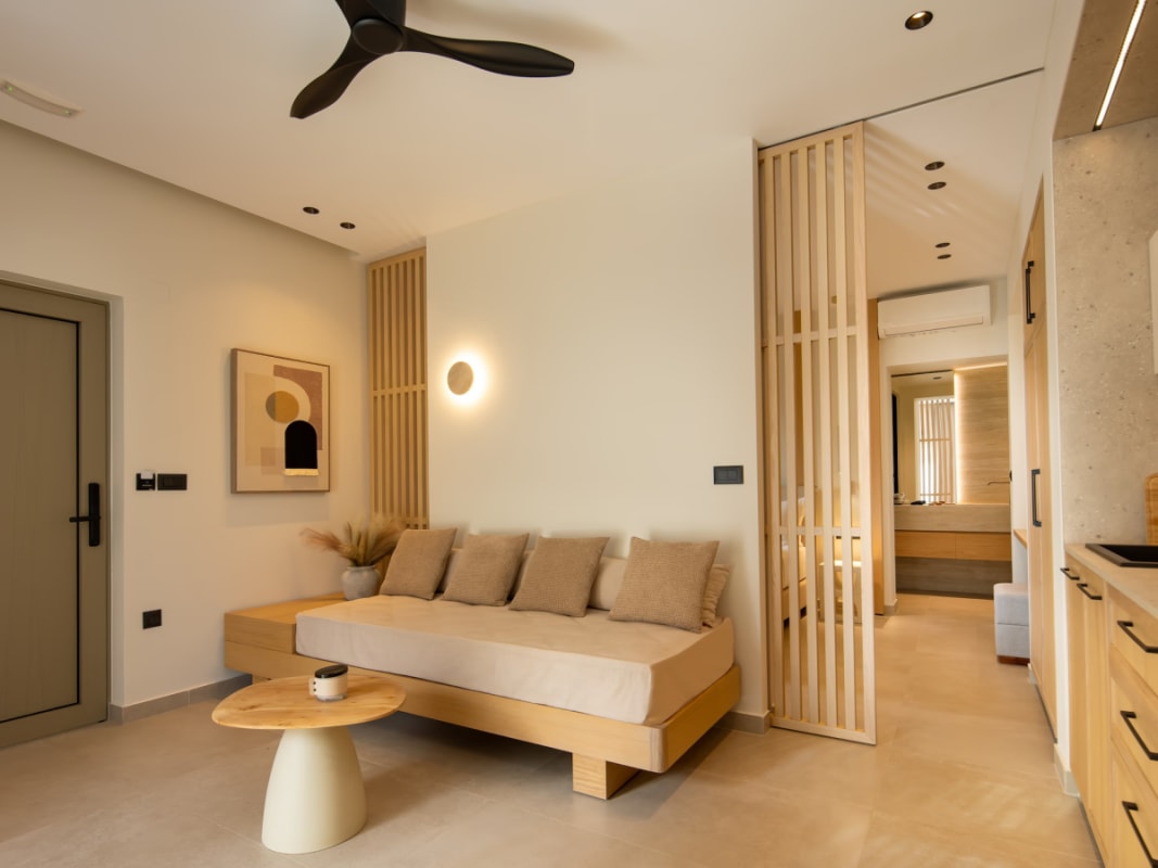 Modern minimalist living room with a neutral sectional sofa, round coffee tables, and illuminated wall shelving.