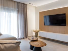 English Modern minimalist living room with a neutral sectional sofa, round coffee tables, and illuminated wall shelving.