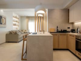 Modern minimalist kitchen with light wood cabinetry, white upper cupboards, and a large island with three wooden bar stools.