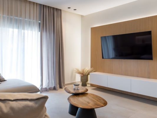 English Modern minimalist living room with a neutral sectional sofa, round coffee tables, and illuminated wall shelving.