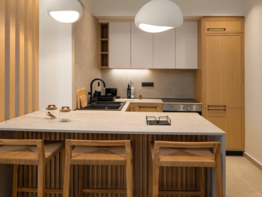 Modern minimalist kitchen with light wood cabinetry, white upper cupboards, and a large island with three wooden bar stools.