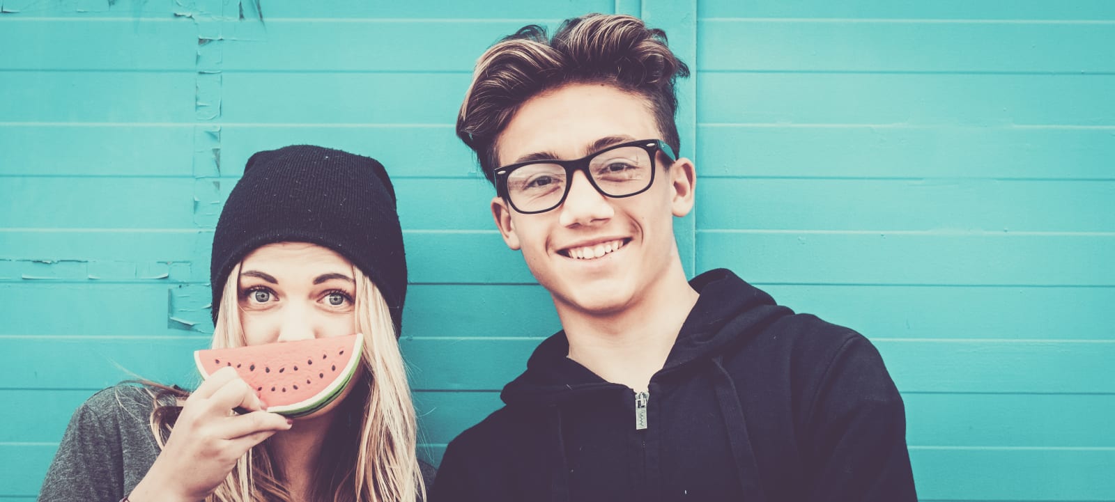 Fun young couple taking a selfie against a turquoise wall with watermelon, representing authentic relatable content from real people