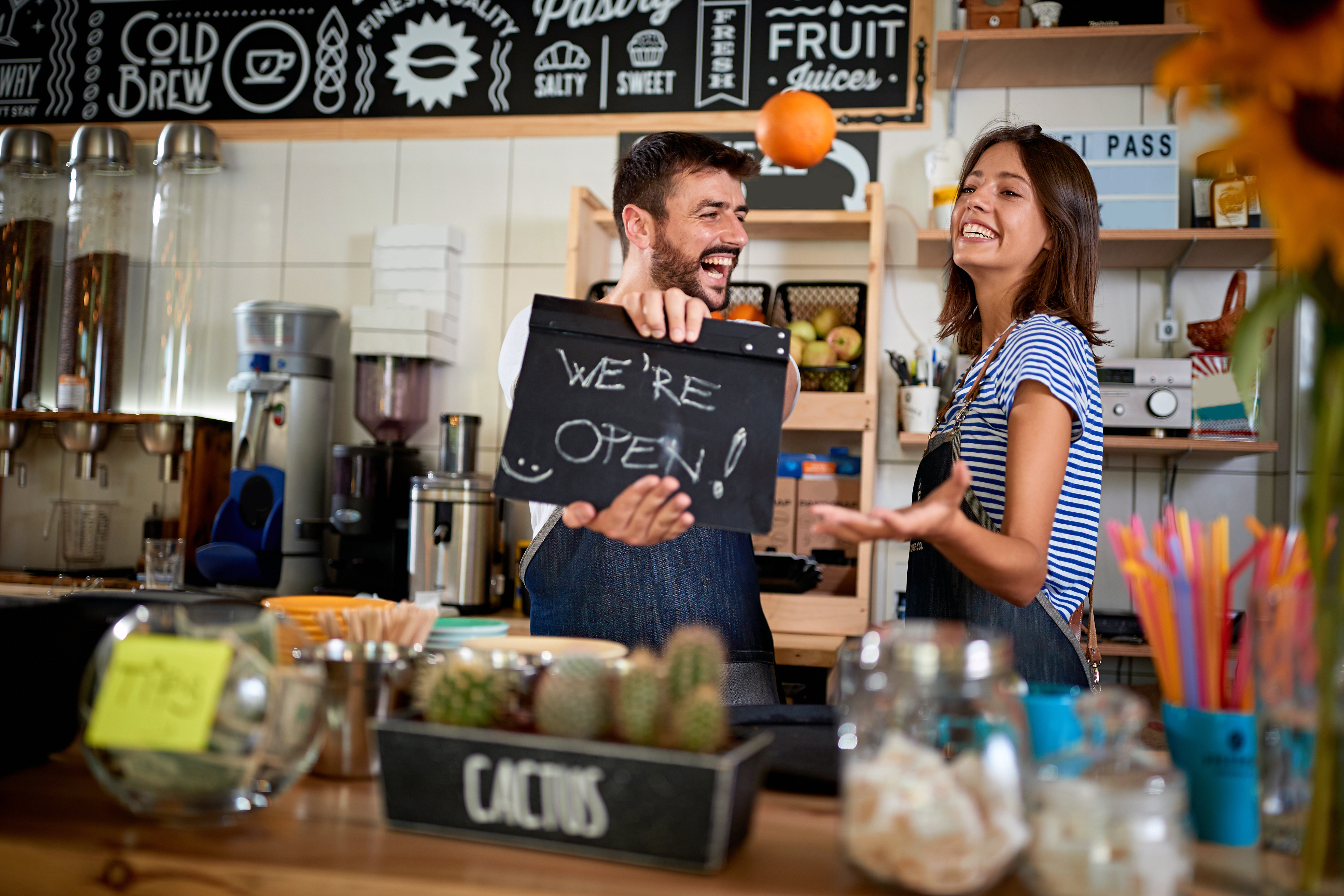 Happy cafe owners behind counter with We're Open chalkboard sign — small food businesses thriving with micro-influencer marketing
