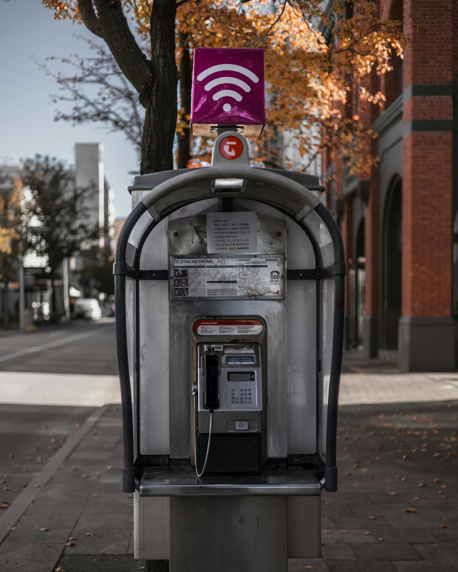 An old payphone on a street corner topped with a modern WiFi sign