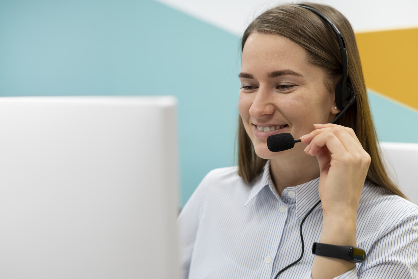 Customer support agent wearing a headset, smiling while looking at her computer screen