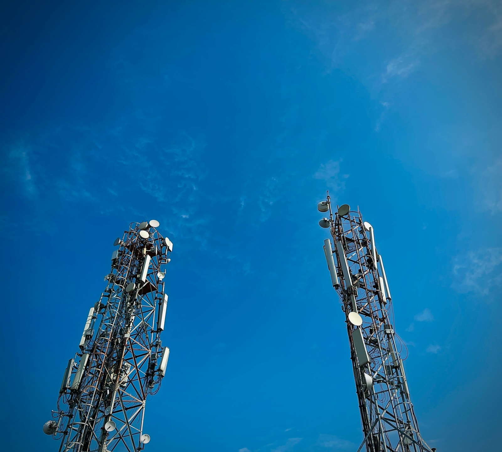 Two cellular towers side by side against a clear blue sky