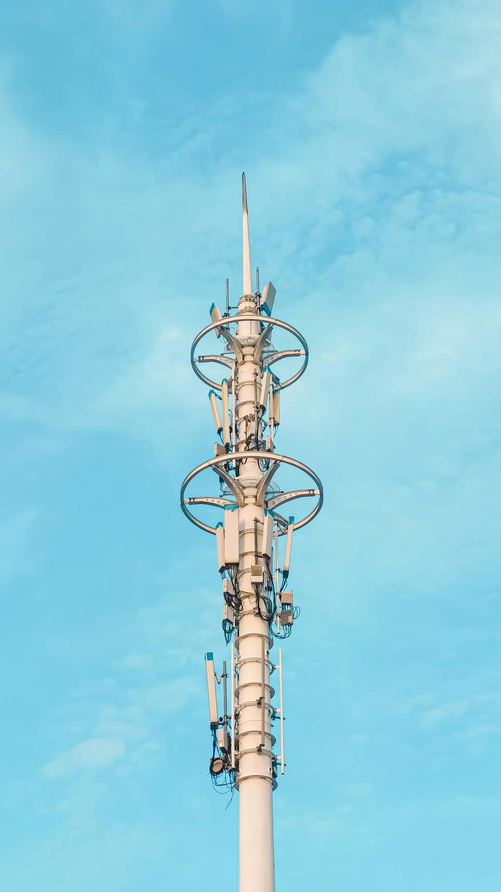 Modern white cellular tower with a circular antenna array against a pale blue sky