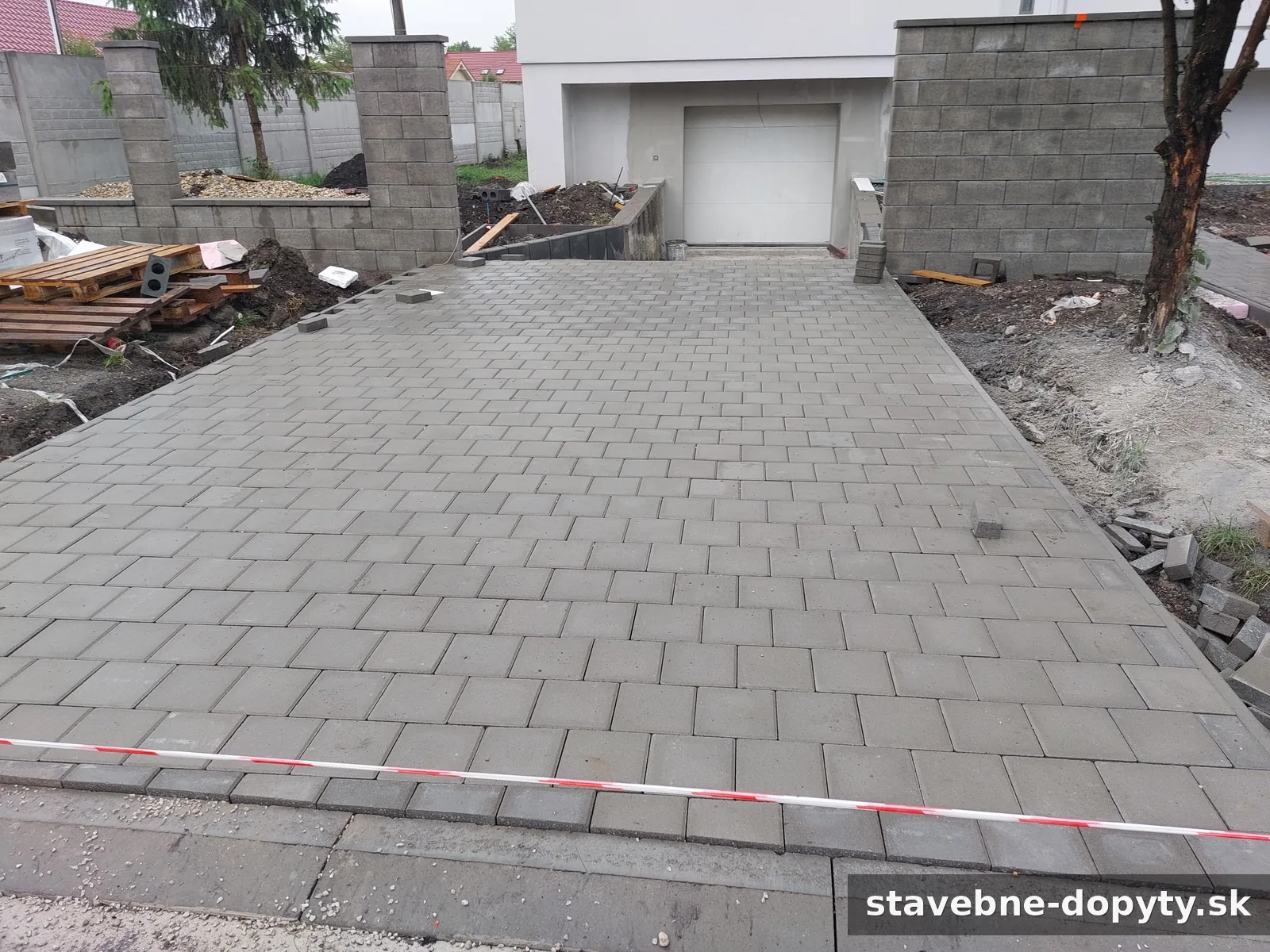 Novopoložená sivá zámková dlažba pred garážou rodinného domu, okolie sa dokončuje.