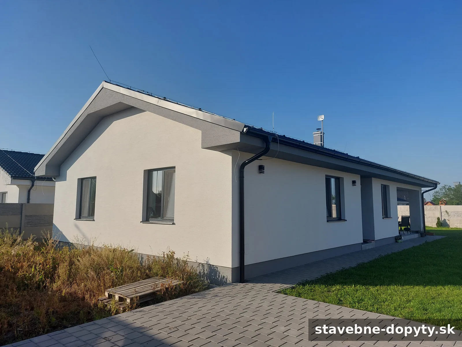 Práve dokončený moderný bungalov s bledou fasádou a tmavou strechou na slnečnom pozemku.
