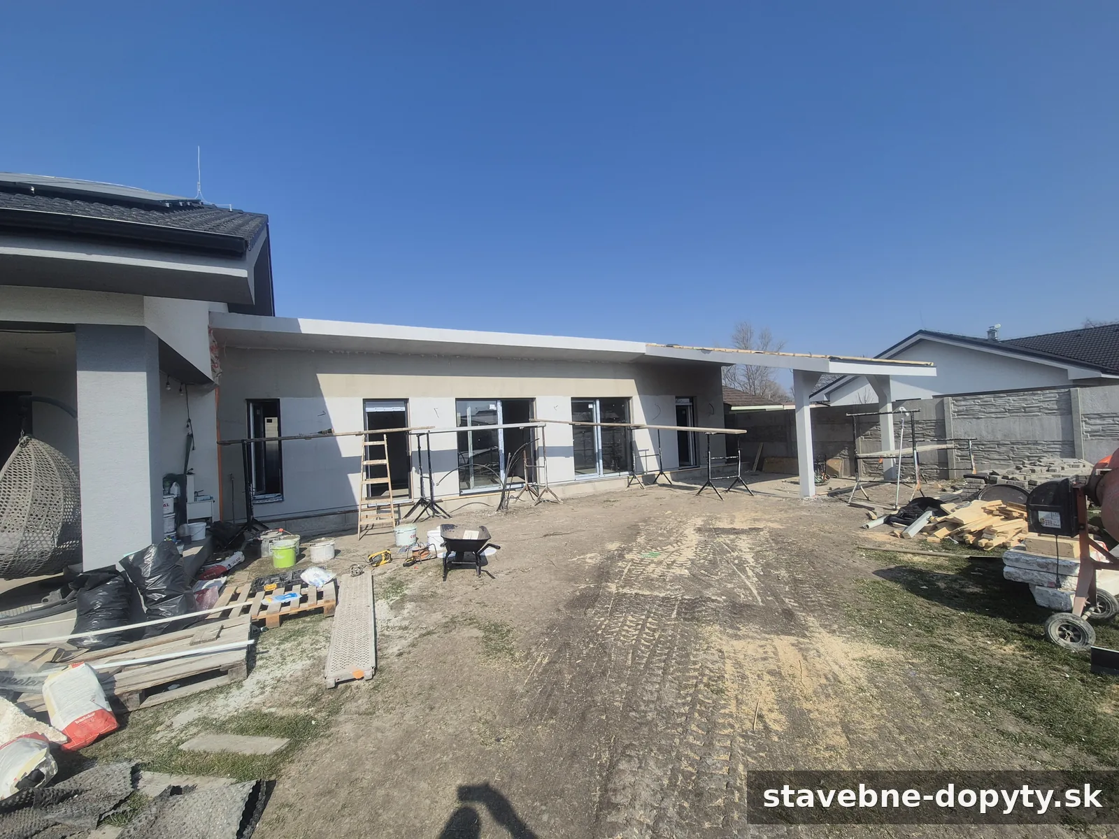 Novostavba moderného rodinného domu s dokončovanou fasádou a rozostavaným prístreškom pre auto.