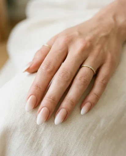 One hand with medium almond nails showing a smooth gradient from warm nude at the cuticle to soft white at the tip, on a cream background One hand with medium almond nails showing a smooth gradient from warm nude at the cuticle to soft white at the tip, on a cream background