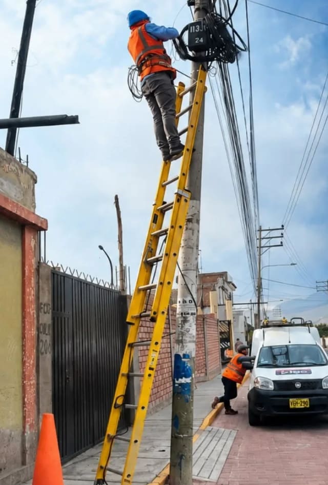 Técnico de Digo sobre una escalera trabajando en la caja de fibra de un poste; abajo, otro técnico junto a la camioneta de Digo
