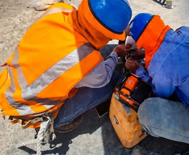 Dos técnicos con casco y chaleco naranja fusionan fibra óptica con una empalmadora