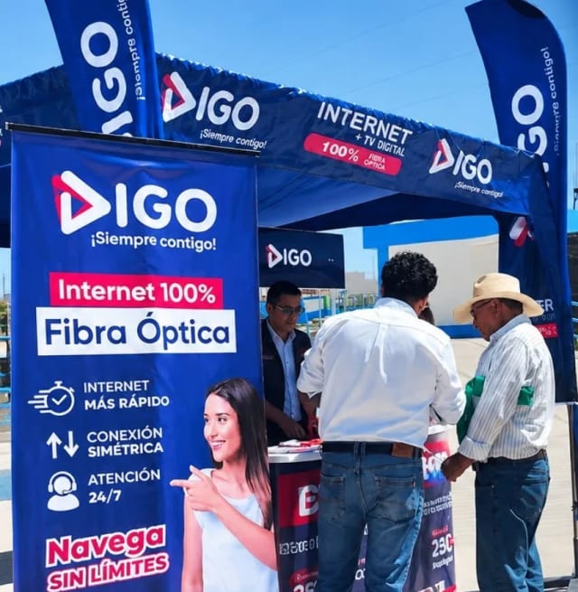Stand de Digo Telecom con banderas y banners, un asesor atiende a dos vecinos