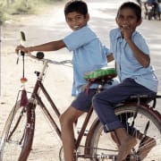 2 Asian boys riding a bike on a dirt road smiling