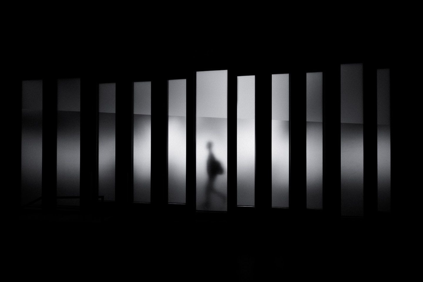 A blurred silhouette of a person reflected in vertical panels on a dark background.