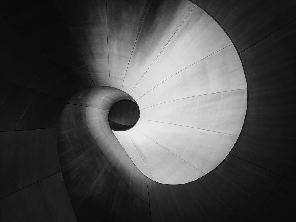 Abstract black and white photo of a brightly lit spiral staircase leading into darkness.