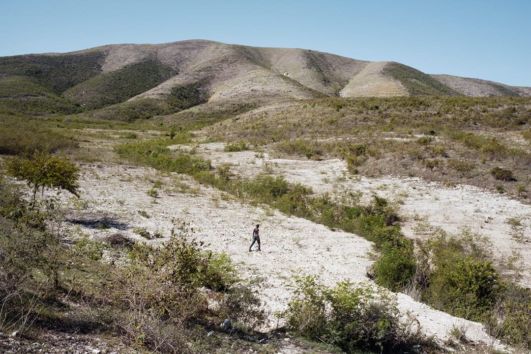 Haiti, Artibonite department. On the outskirts of Les Gonaïves, a young man is walking through a deforested landscape. Hai...