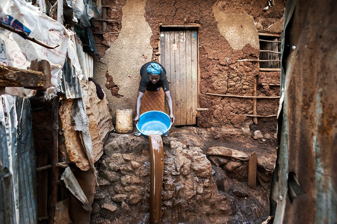 Nairobi, Kenya. Rose, 34 years old, is spilling dirty water outside her hut in Kibera. She is an environmental migrant, wo...