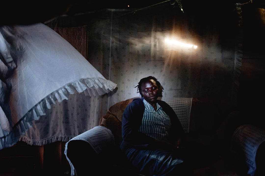 Nairobi, Kenya. Sharon, a climate migrant, sits on the sofa in her iron hut in Kibera with her two children. She emigrated...