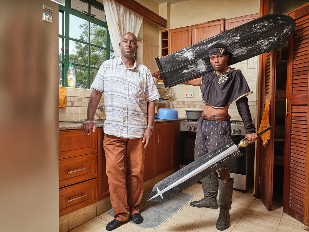 10/01/2024 
Francis (29) poses with his father in their kitchen, Nairobi. 
A tech and fitness freelancer and cosplayer sin...
