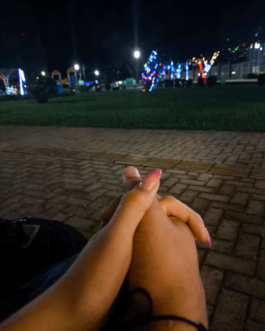 Las manos de los dos entrelazadas de noche, con las luces de navidad del parque al fondo