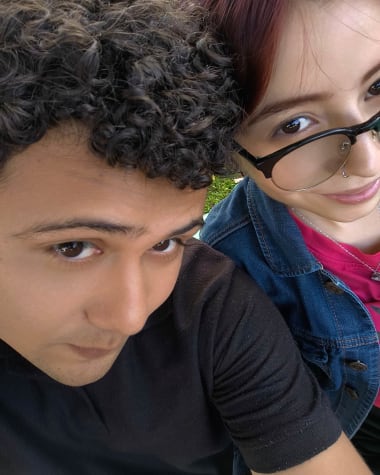 Katheryn con chaqueta vaquera y Brandon sentados sobre el cesped de un parque