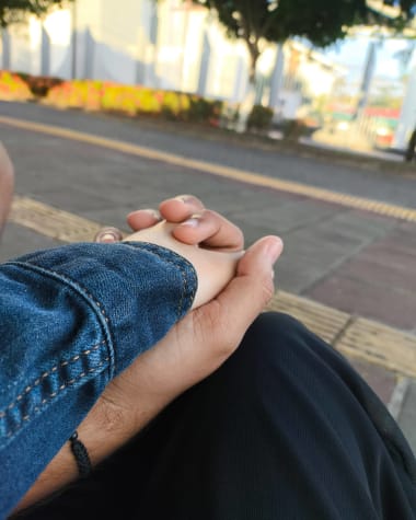 Las manos de los dos entrelazadas sobre la rodilla, en la calle a plena luz