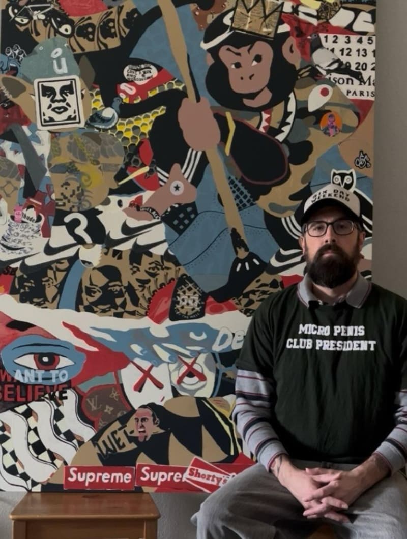 Chris Maye seated in front of one of his large sticker collage paintings.