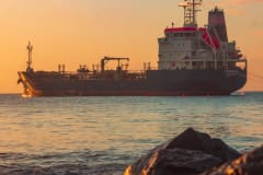 Large oil tanker on the ocean near the coast, sailing under a vibrant sunset sky.