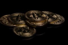 A close-up image of golden Bitcoin coins displayed on a reflective black surface.