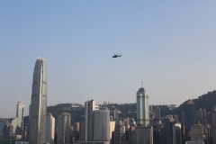 A helicopter flies above the iconic Hong Kong skyline during the day.