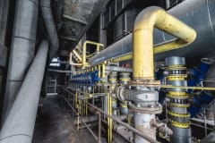 Close-up of an intricate industrial pipeline system featuring yellow valves and steel structures inside a factory.