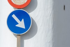 Close-up of a blue downward arrow sign on a white wall, symbolizing direction and caution.