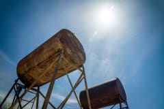 Rusty industrial oil tanks with a clear blue sky and bright sun.