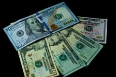 Detailed view of multiple US dollar bills against a black background, highlighting financial themes.