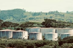 Large industrial storage tanks set amidst a verdant and hilly landscape.